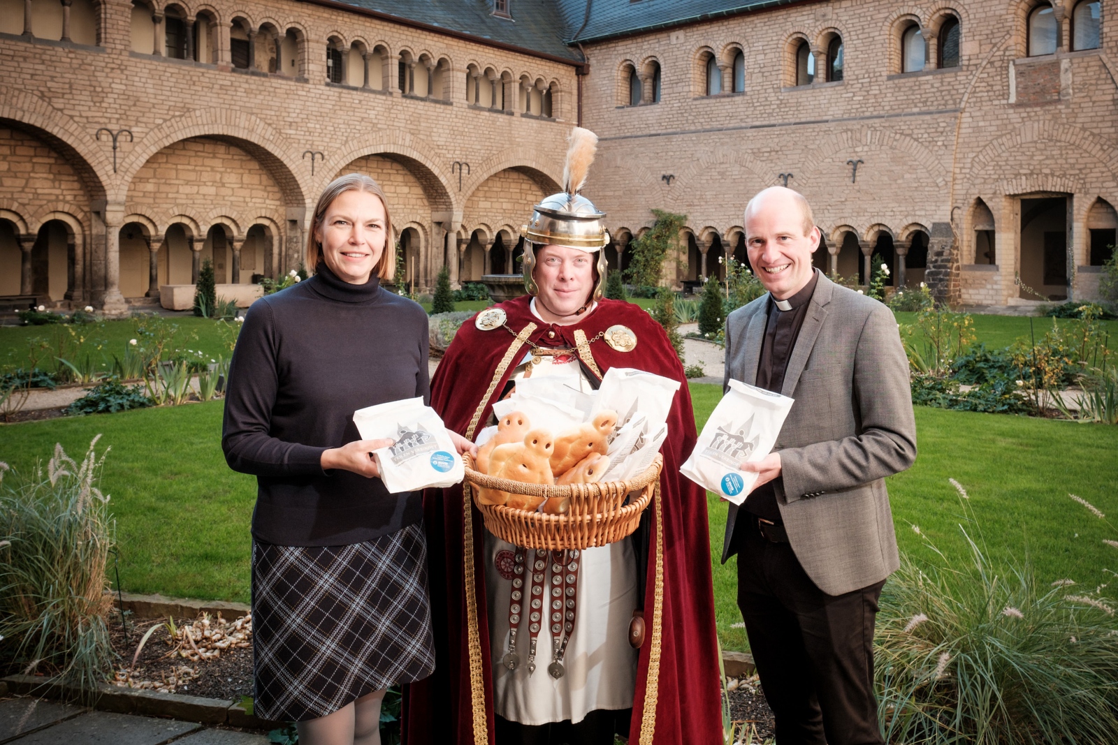 Lisa Pias, Fachbereichsleiterin Marketing: Strategie und Digitales bei den Stadtwerken Bonn und Münsterkaplan und Pfarrverweser Dr. Christian Jasper gemeinsam mit dem „St. Martin“ (Martin Heide) bei der symbolischen Übergabe der Weckmänner im Kreuzgang der Bonner Münsterbasilika.